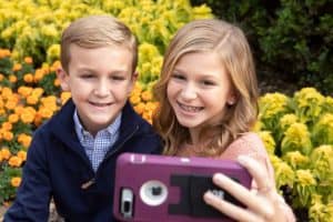 A blond brother and sister taking a selfie in a park