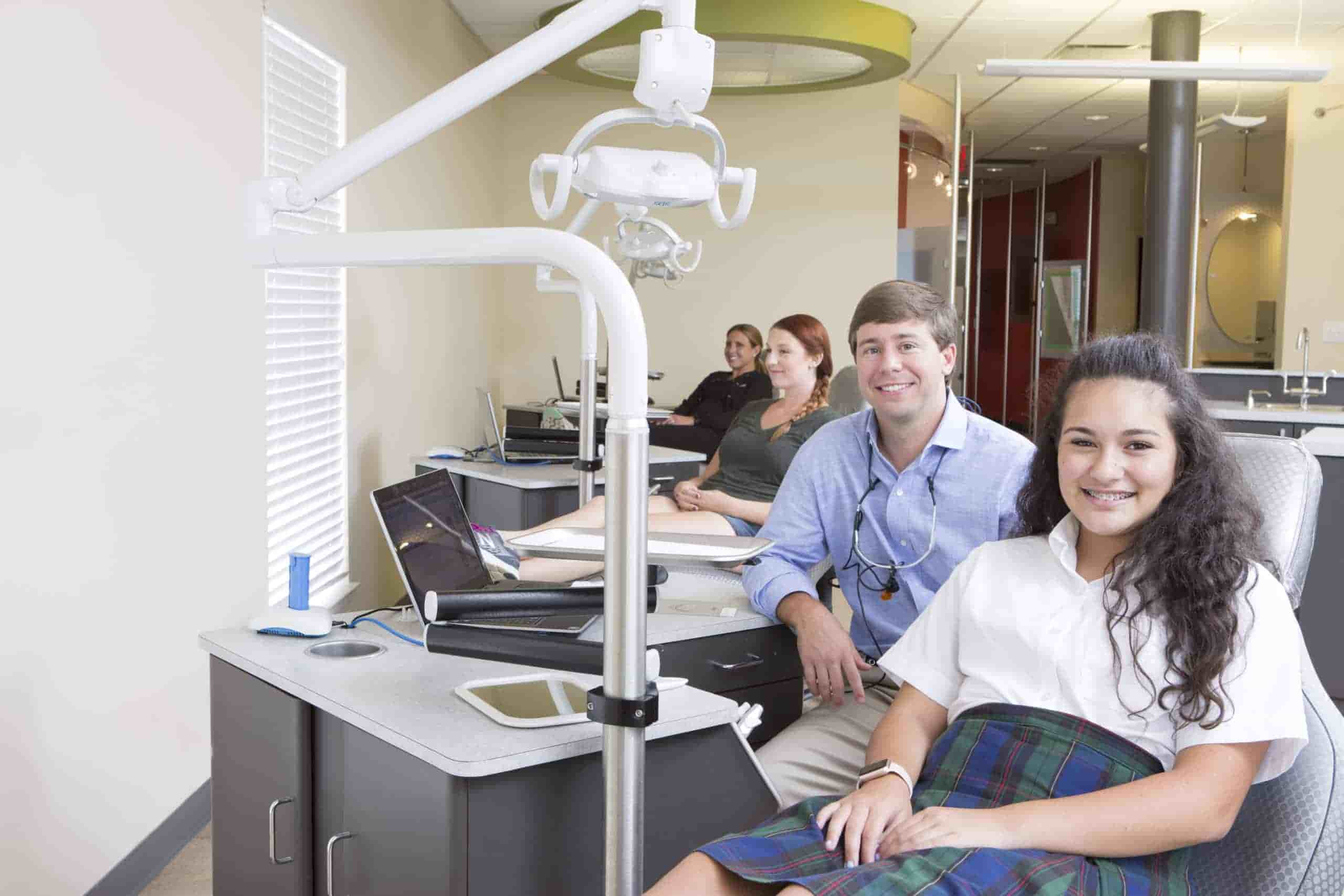 An orthodontist and three teenagers in treatment chairs smiling at the camera