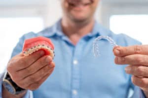 Close up of a man holding a model of teeth with braces and a clear aligner