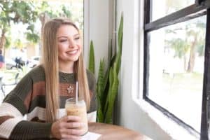 Teenage girl with straight blond hair holding an iced coffee and looking out the window